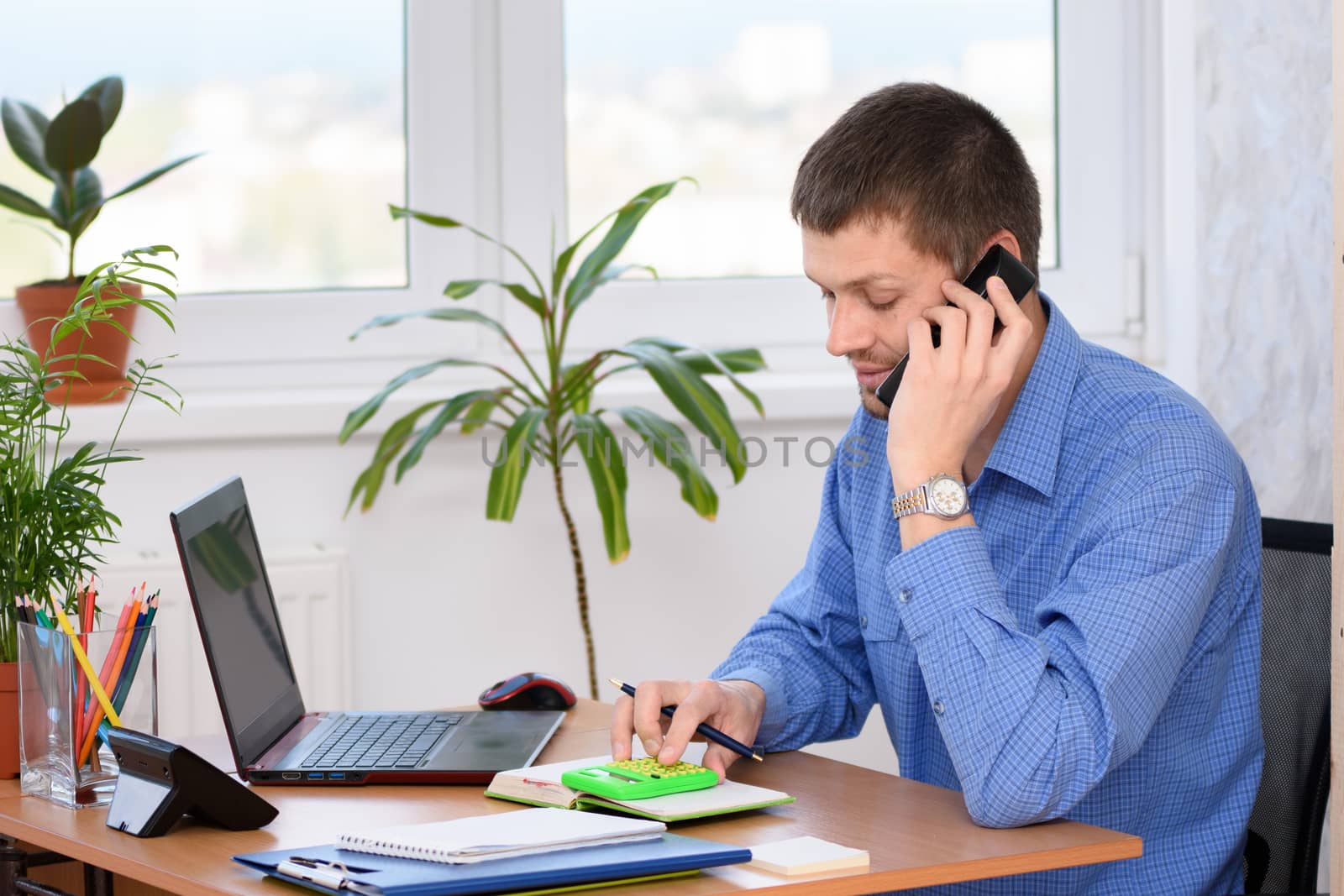 An office employee is smiling on the phone and counting on a calculator