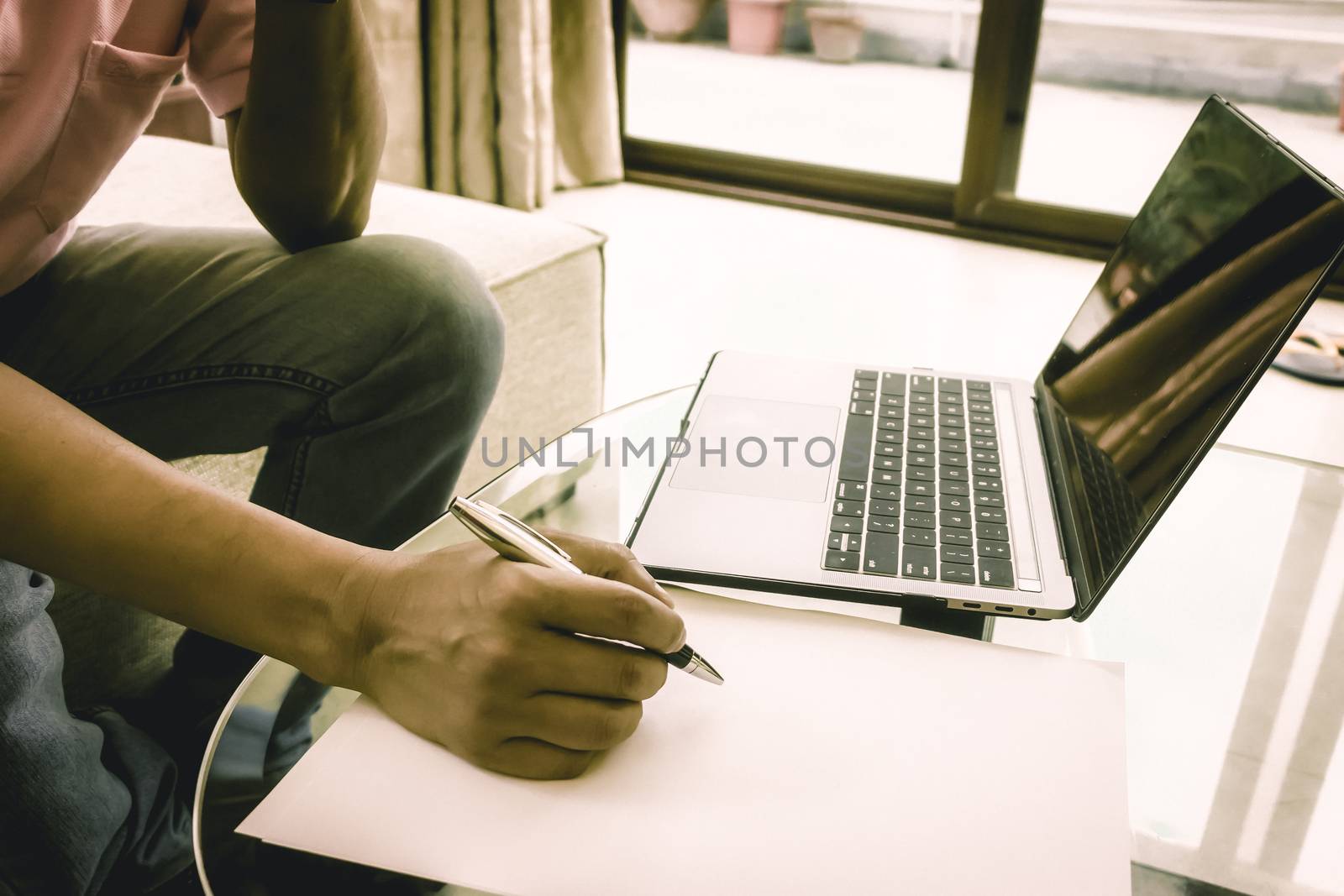 Anonymous Worker writing on a sheet of paper a business project work on office desk. Laptop is placed on the table. Side view. Close-up. Vintage style effect. Copy space room for text.
