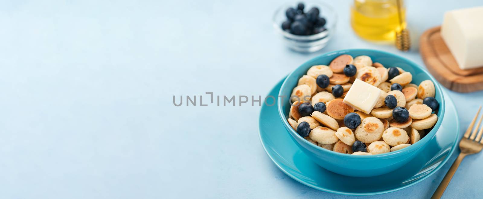 Trendy food - pancake cereal. Heap of mini cereal pancakes in boul on blue background. Copy space for text or design. Long horizontal banner
