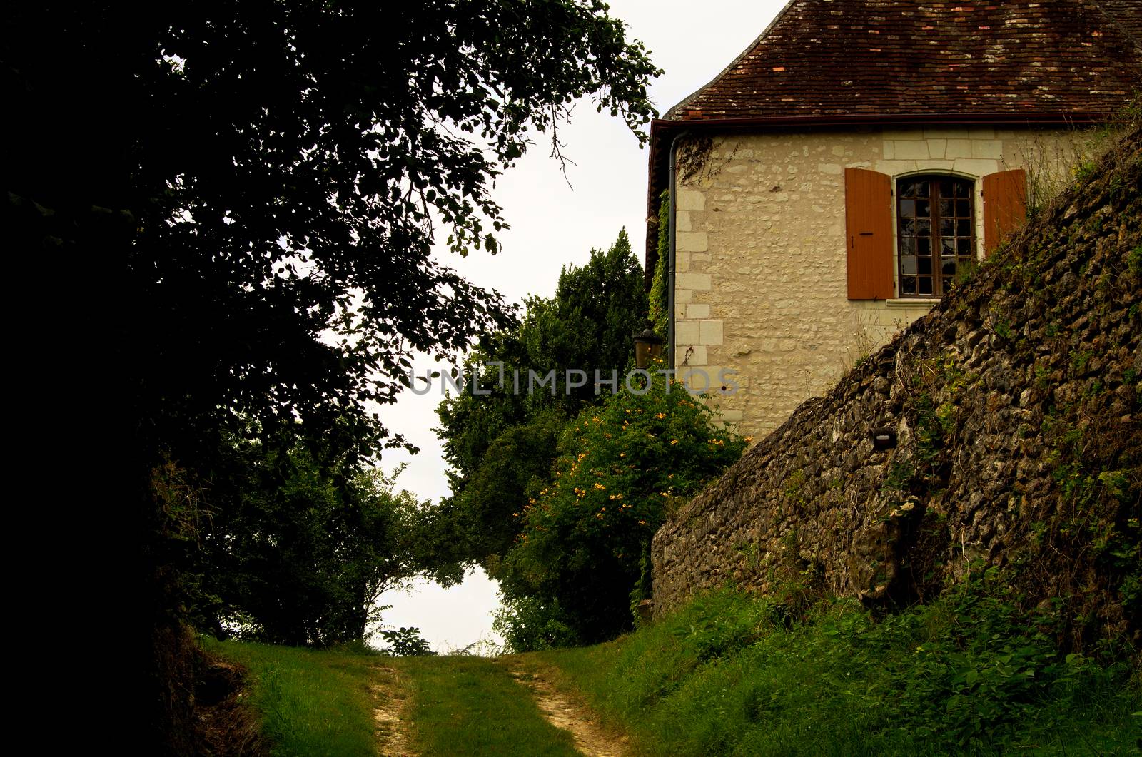 Rural scene in the Indre region of France, with a track running up past the farmhouse shaded by tree cover