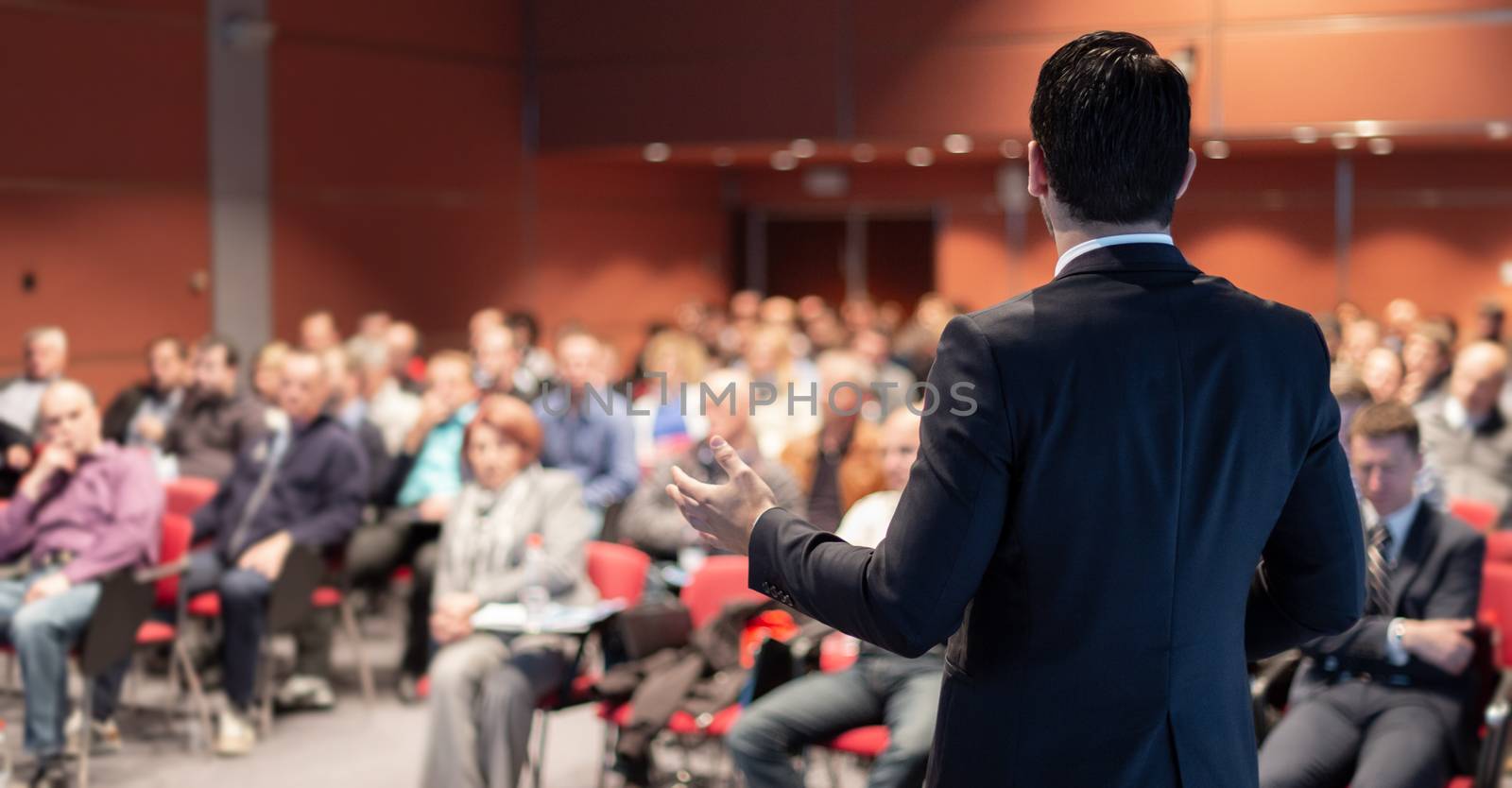 Speaker giving a talk on corporate business conference. Unrecognizable people in audience at conference hall. Business and Entrepreneurship event.