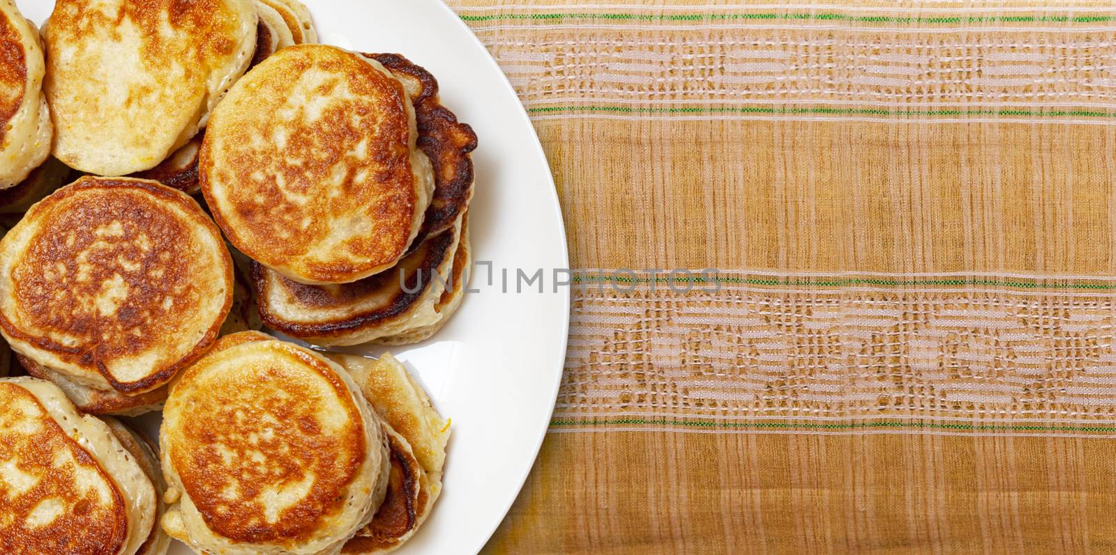 CHISINAU, MOLDOVA - May 18, 2020: Pile of freshly baked pancakes lay on a white plate on a folk embroidery fabric handmade close up. Top view