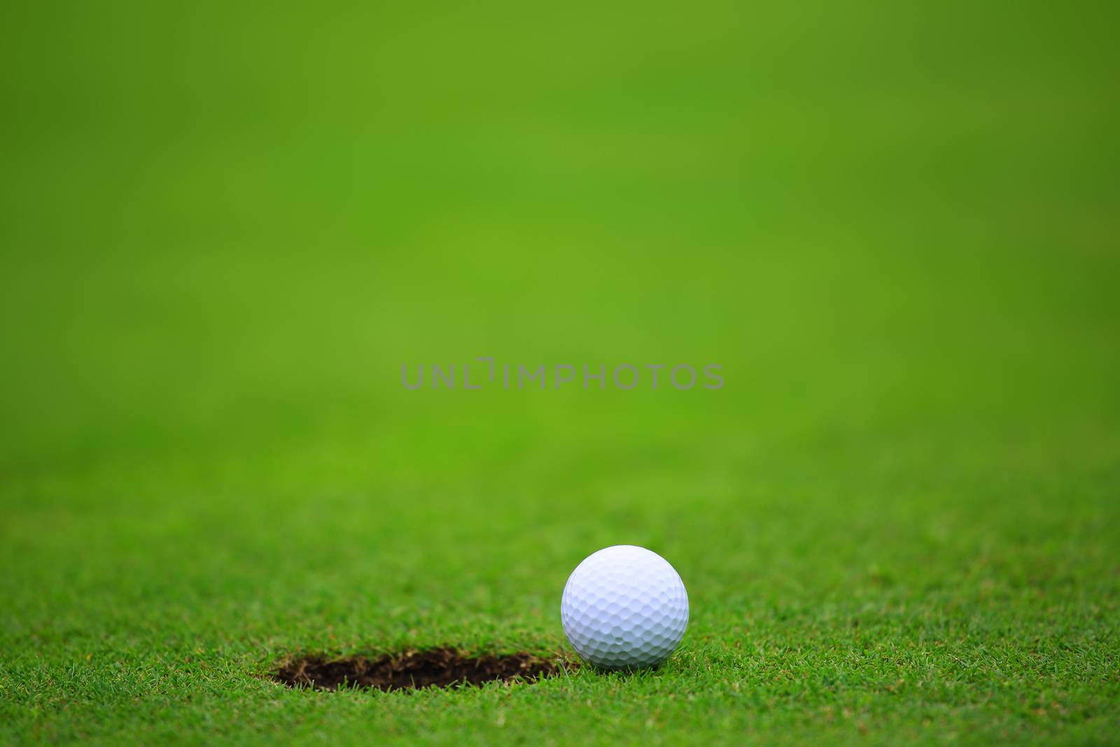 Golf ball close to hole, on lip of cup on green of golf course background with copy space for text banner