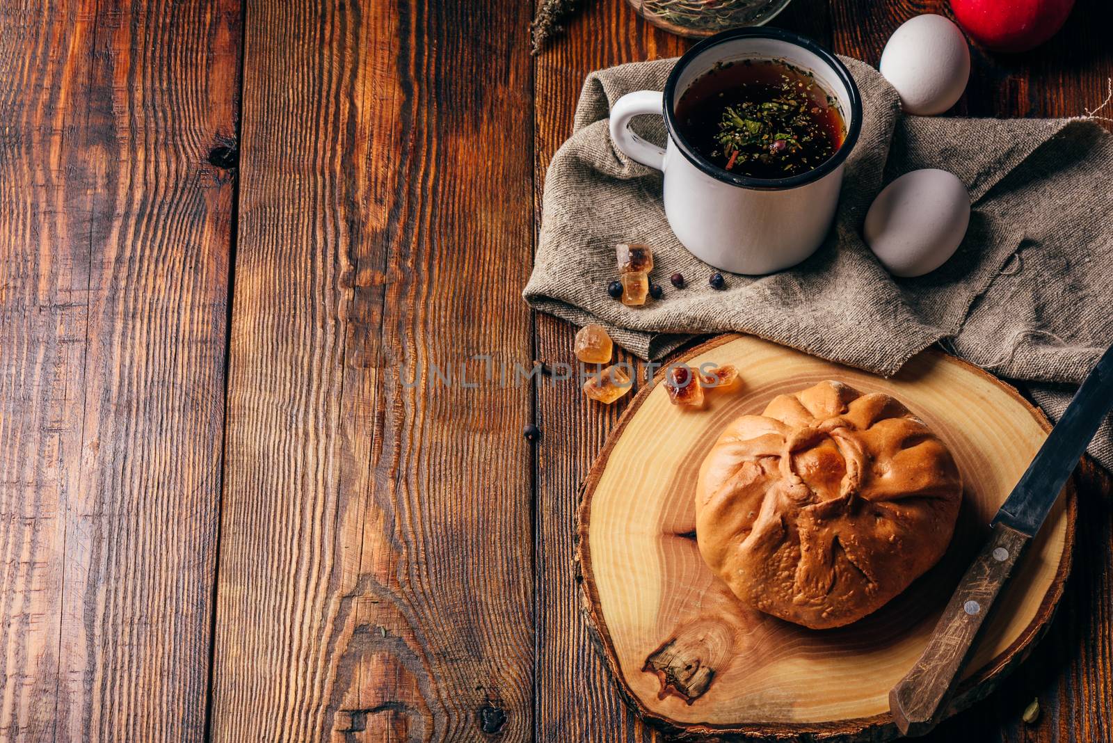 Rustic breakfast with traditional tatar pastry elesh, herbal tea in metal mug, apple and boiled eggs over dark wooden surface