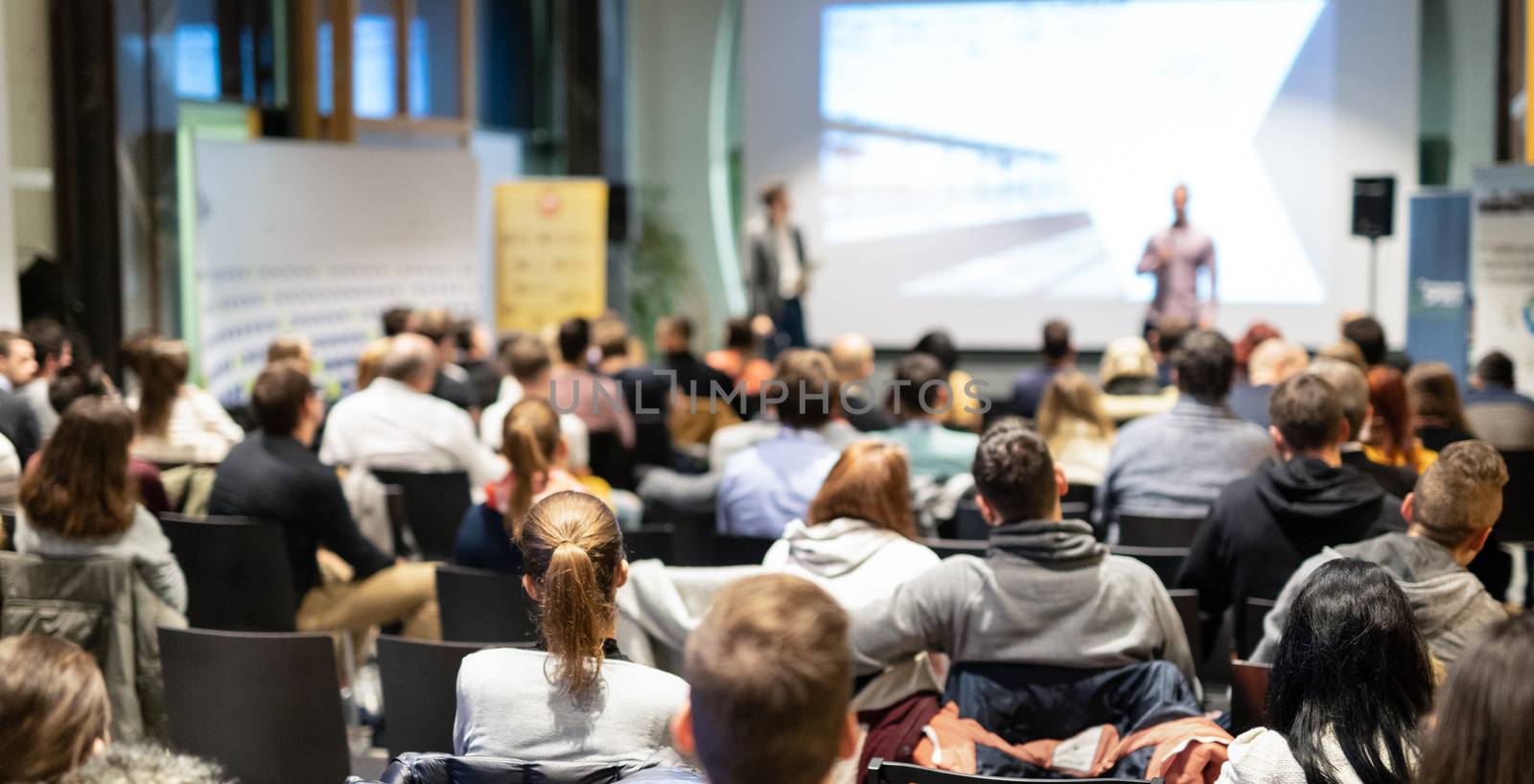 Speaker giving a talk in conference hall at business event. Rear view of unrecognizable people in audience at the conference hall. Business and entrepreneurship concept.