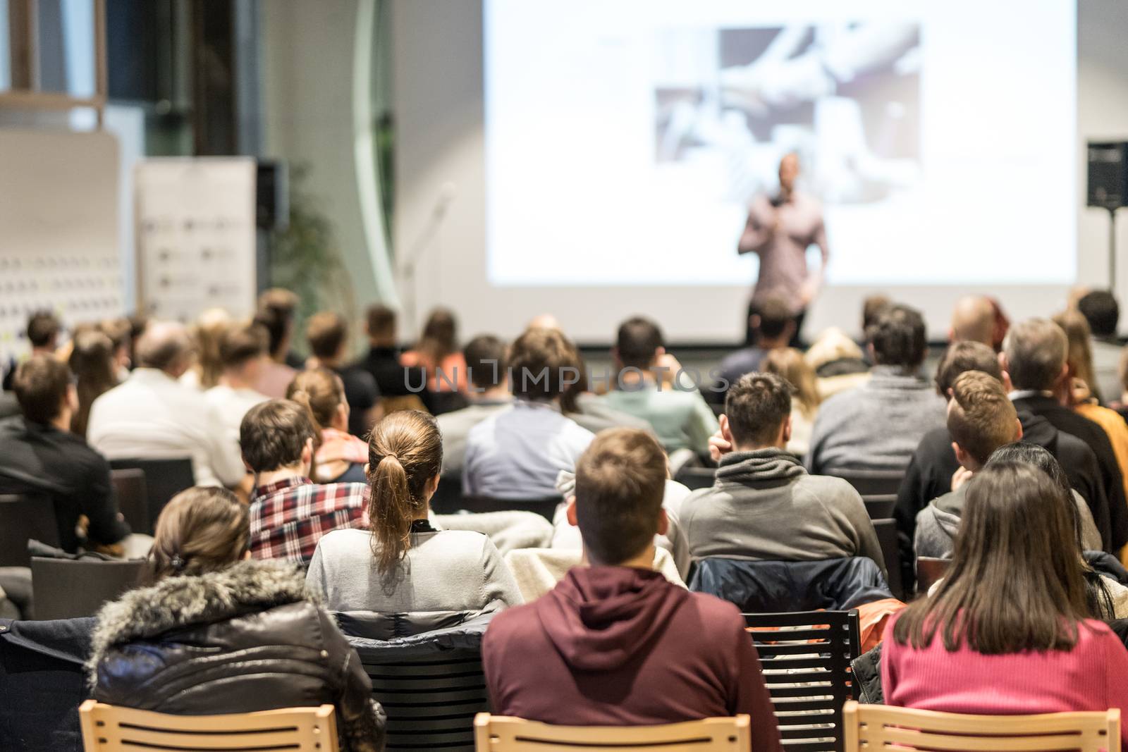 Speaker giving a talk in conference hall at business event. Rear view of unrecognizable people in audience at the conference hall. Business and entrepreneurship concept.