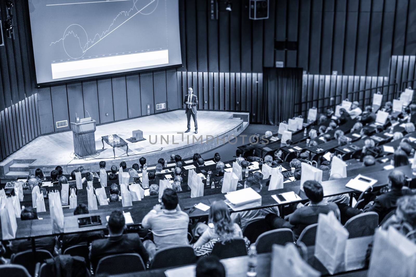Speaker Giving a Talk at Business Meeting. Audience in the conference hall. Business and Entrepreneurship concept. Blue toned.