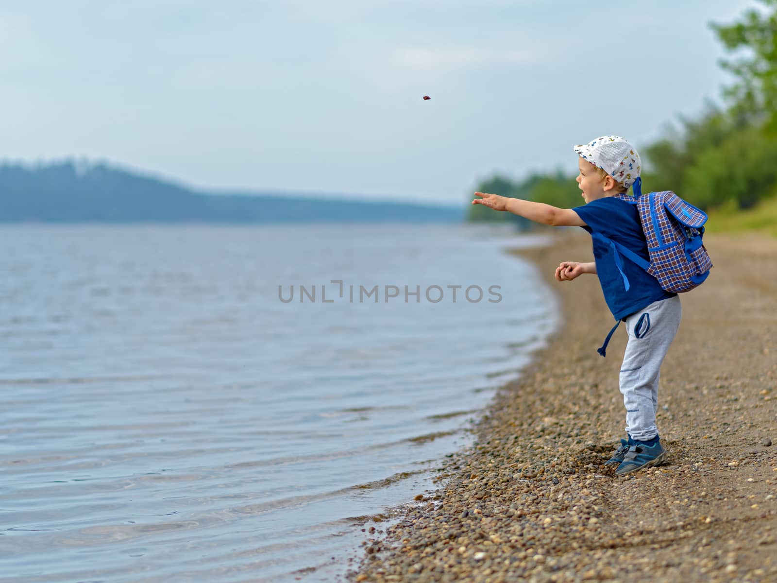 A boy of four years by the river throws stones into the water. by vladali