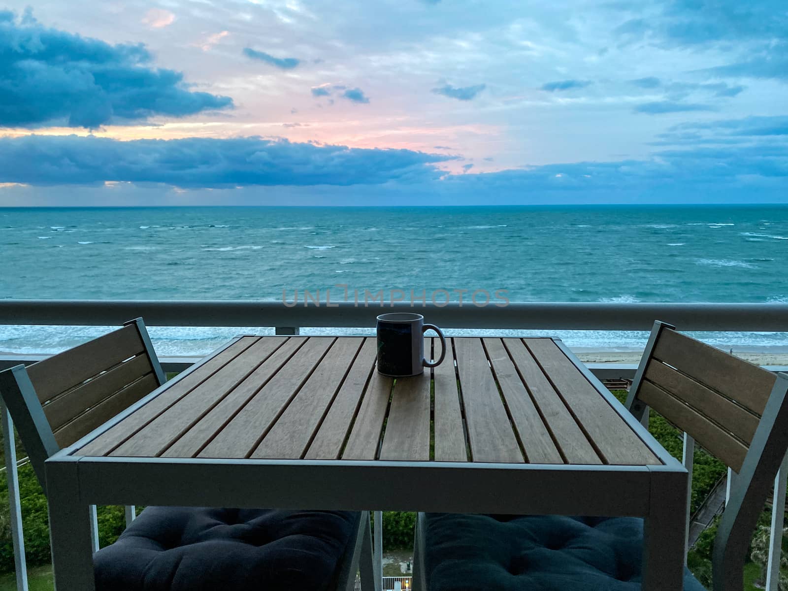 A coffee cup on a table with a vibrant sunrise over the Atlantic Ocean on North Hutchinson Island in Florida in the background.