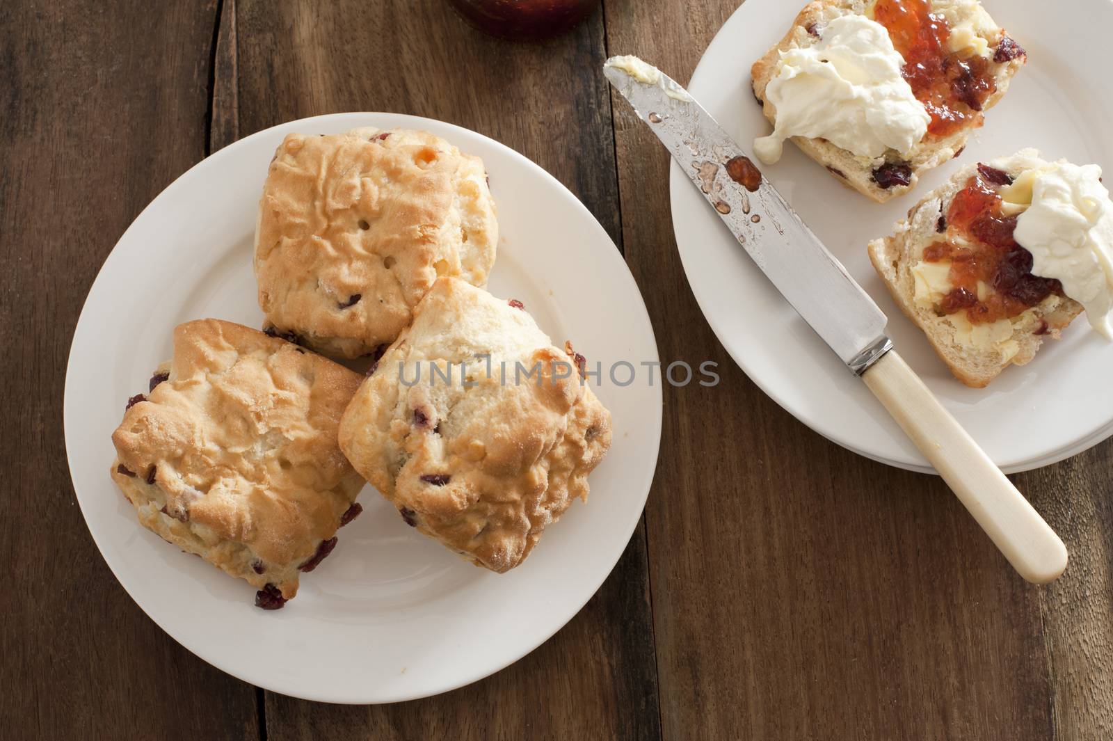 Freshly baked rock cakes or fruit scones on a plate with a single buttered cake alongside with jam and whipped cream