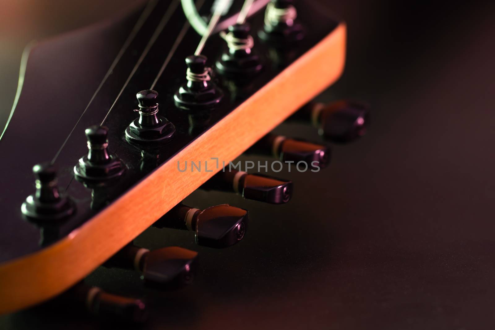 Closeup tuning key on the headstock of the black electric guitar in dark background and morning light. Copy space on the right. Concept of good memory About retro musical instruments and rock music.