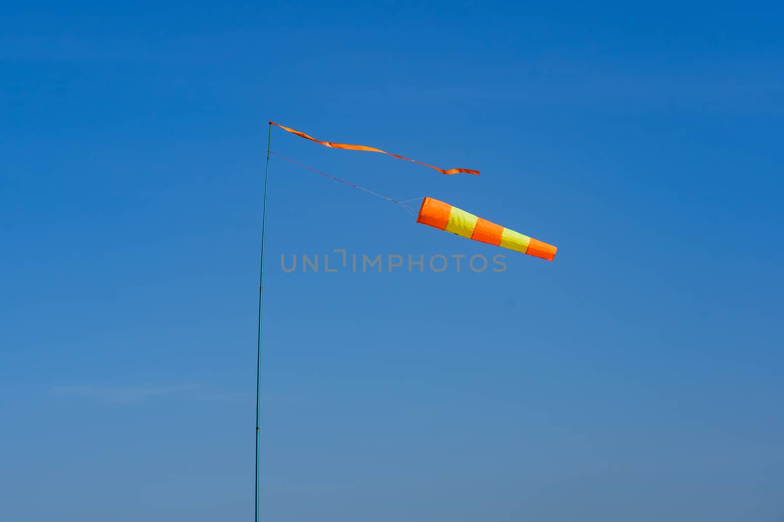 flagpole with wind indicator on a background of blue sky on a windy day