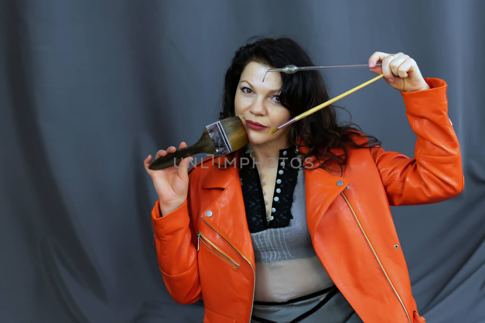 Portrait of a fashionable middle-aged woman in a bright orange leather jacket, posing on a dark gray background by bonilook