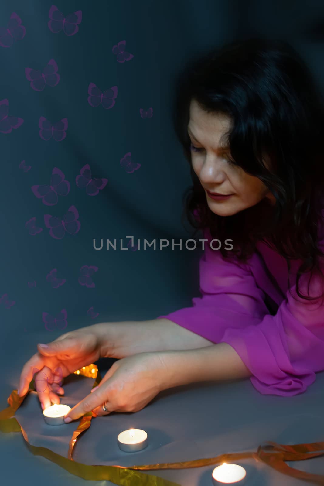 Portrait of a beautiful fashionable middle-aged woman in a bright pink semi-transparent long dress, posing on a dark gray background.