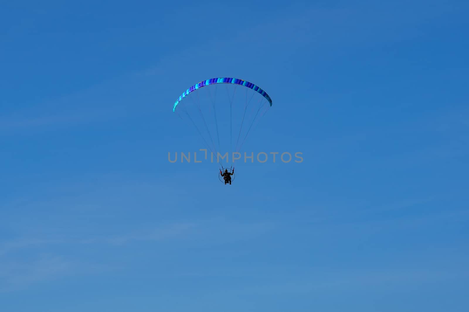 paraglider with a blue parachute flies against a cloudless blue sky