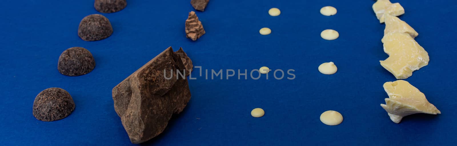 Pieces of natural dark chocolate and white chocolate on a blue background