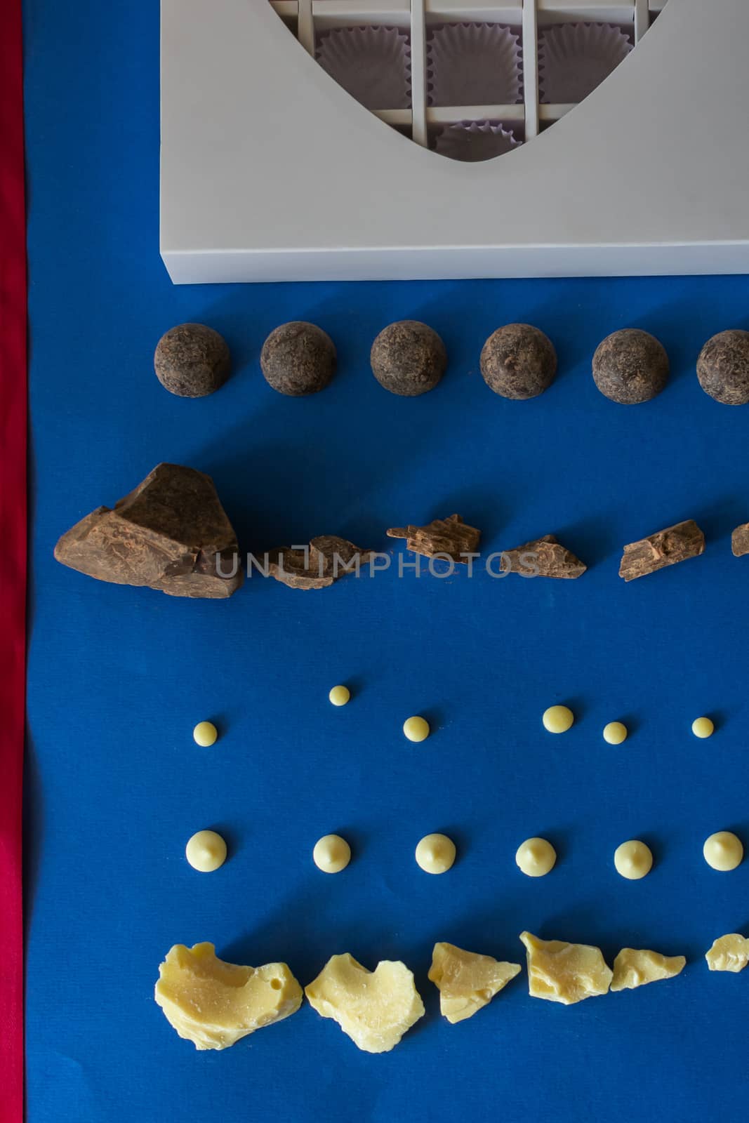 Pieces of natural dark chocolate and white chocolate, a white heart - shaped box of chocolates and a red ribbon lie on a blue background