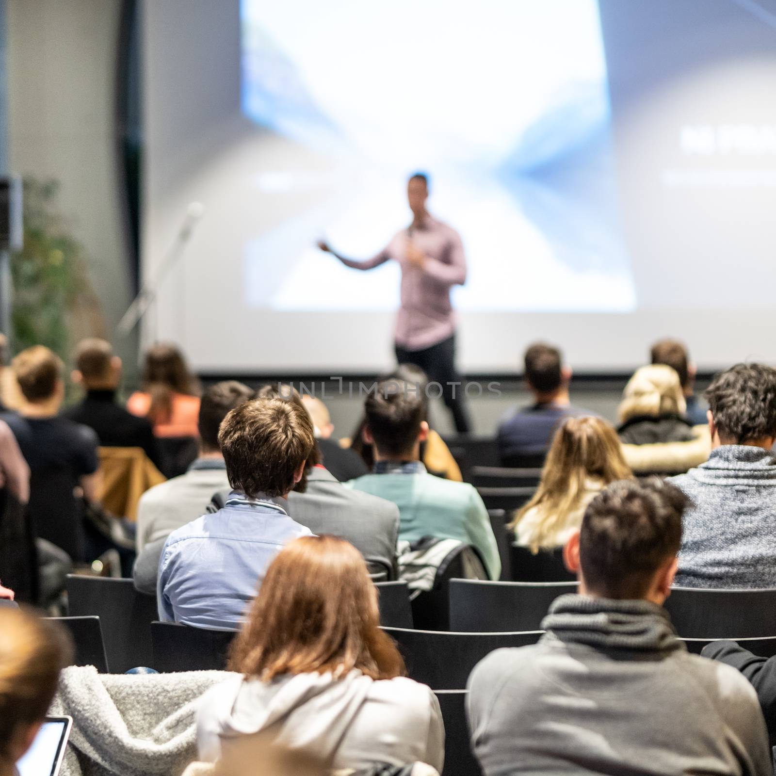 Speaker giving a talk in conference hall at business event. Rear view of unrecognizable people in audience at the conference hall. Business and entrepreneurship concept.