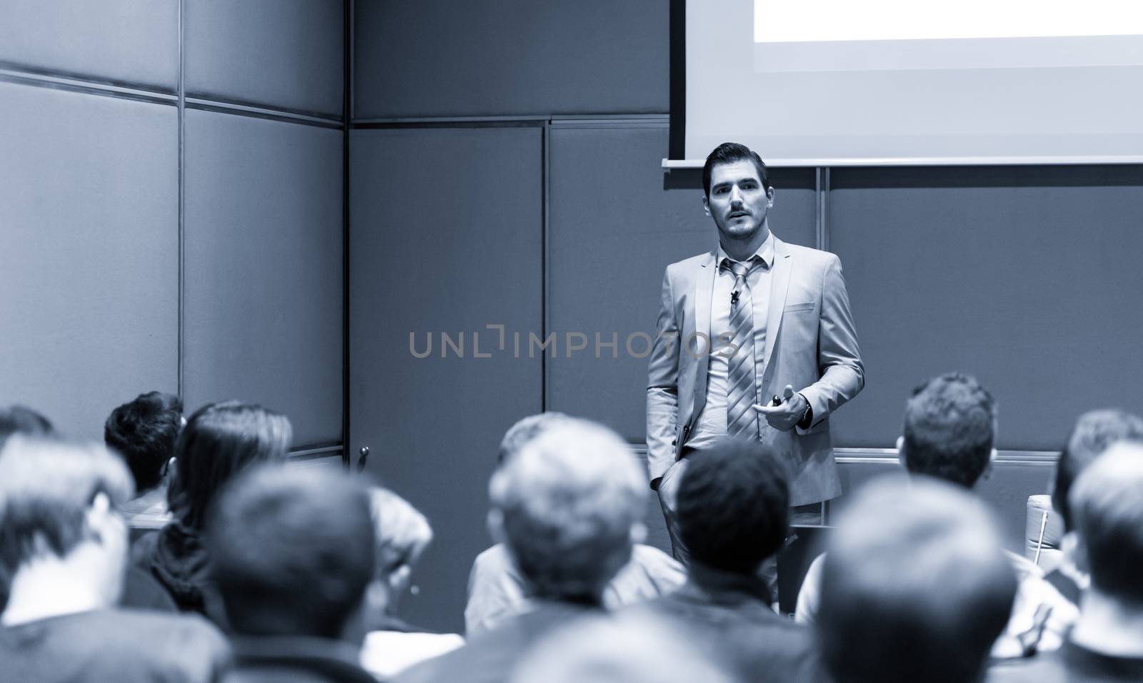 Speaker giving a talk in conference hall at business meeting event. Rear view of unrecognizable people in audience at the conference hall. Business and entrepreneurship concept.