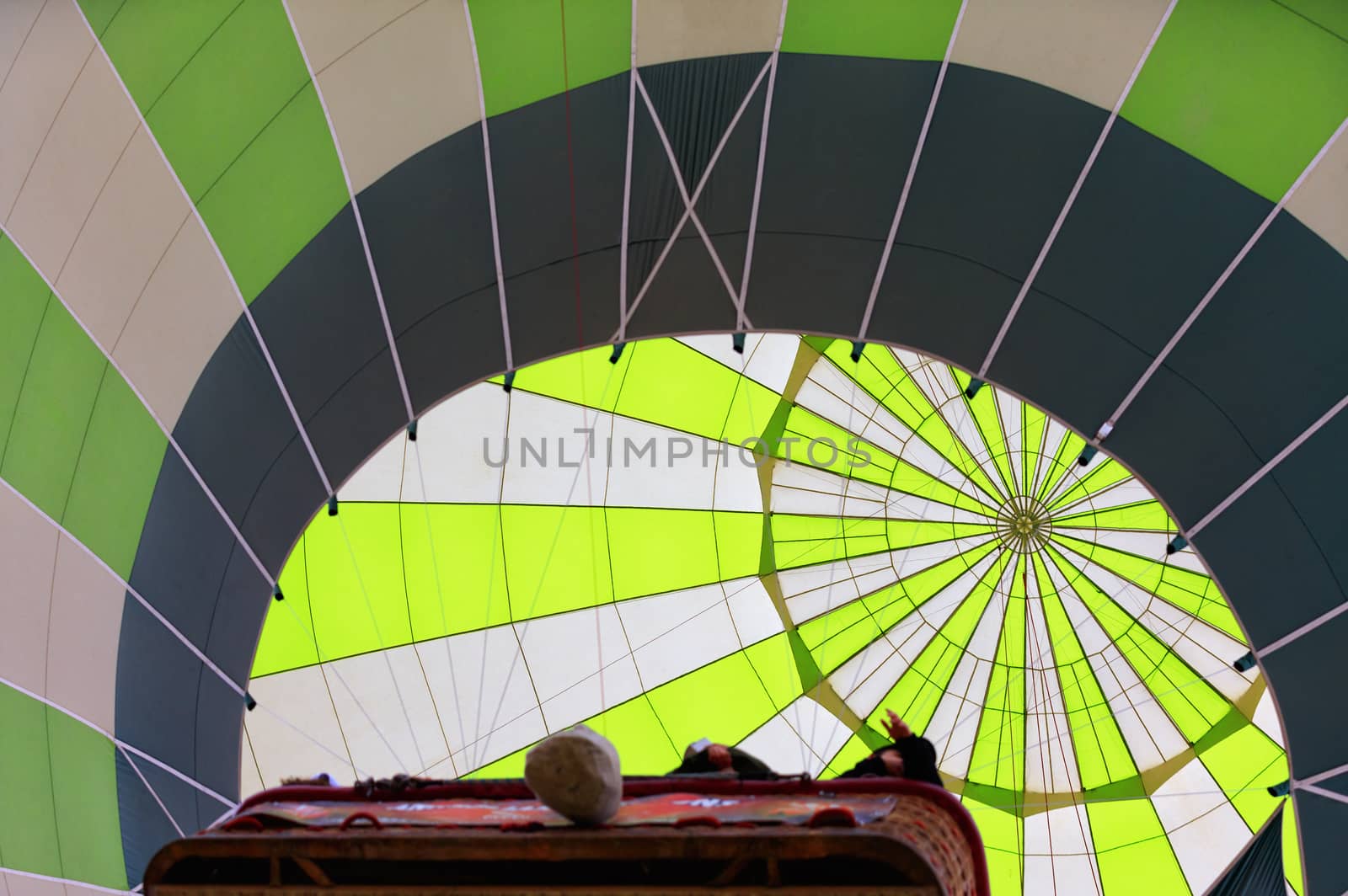 Radial grooves in the center of a bright dome of a white-green balloon that lifts people in a wicker basket.