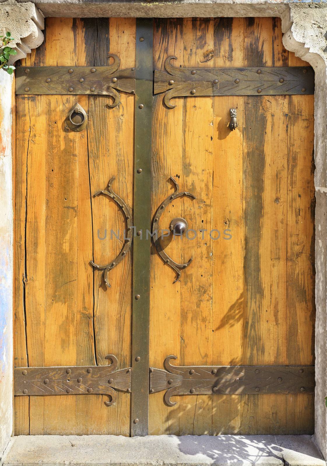 Antique massive wooden doors with wrought handles, rivets and crossbars illuminated by bright sunshine.