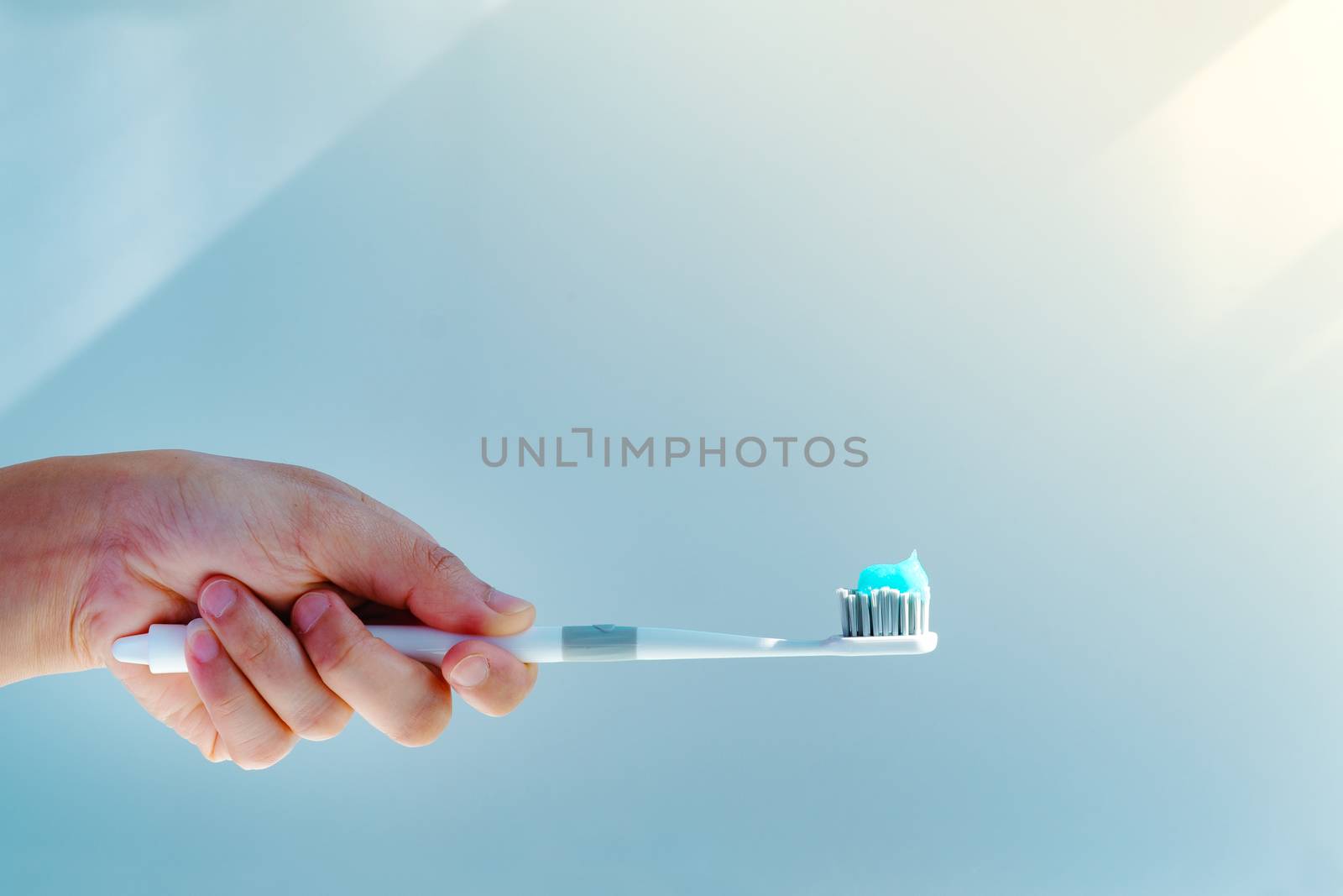 Woman hand holding toothbrush with toothpaste applied on. Closeup of  white toothbrush with blue tooth paste