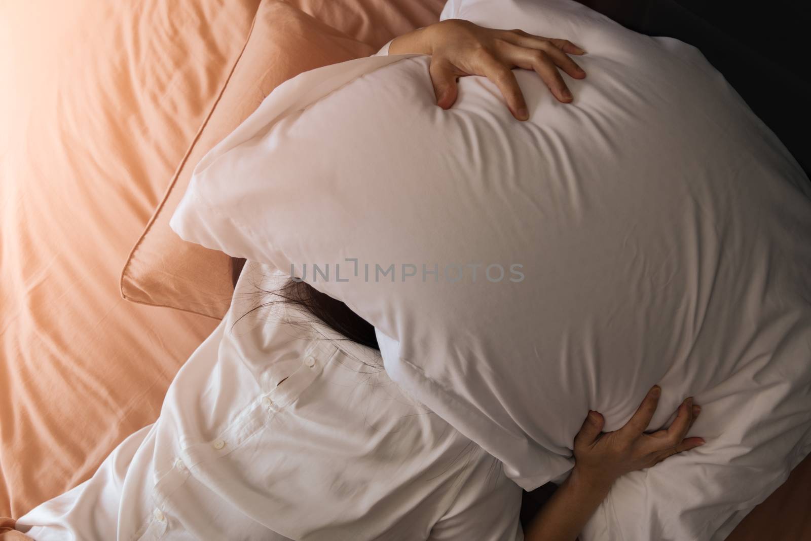 Sleepy woman hide under the pillow hates waking up early in the morning