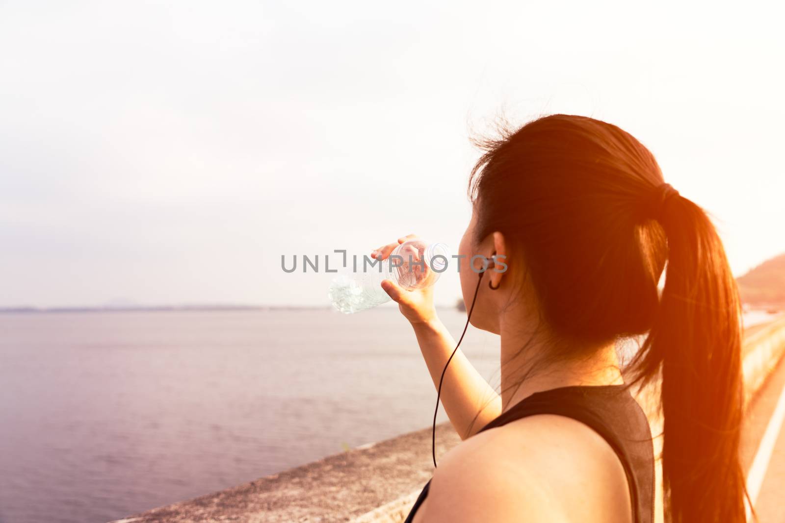 Sport woman standing on the bay and drinking water after running