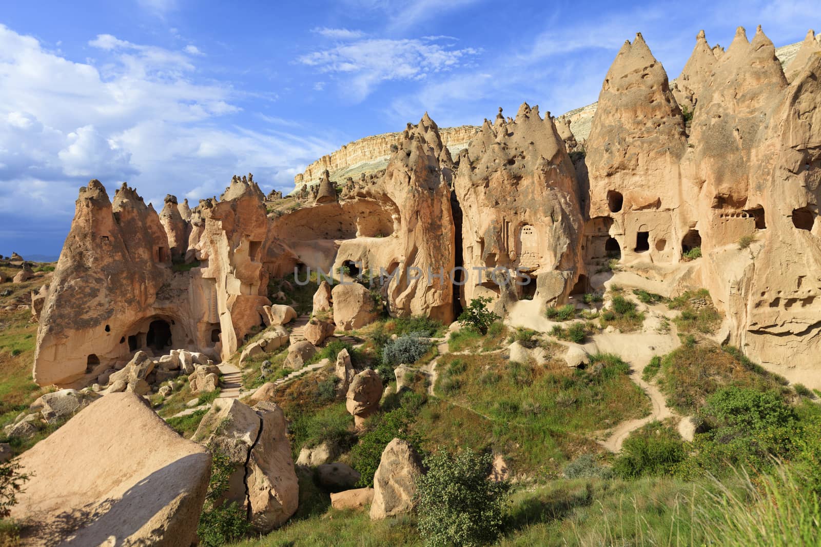 Old ancient city of red sandstone under the open blue sky, residential caves on the background of the conical ridges of Cappadocia