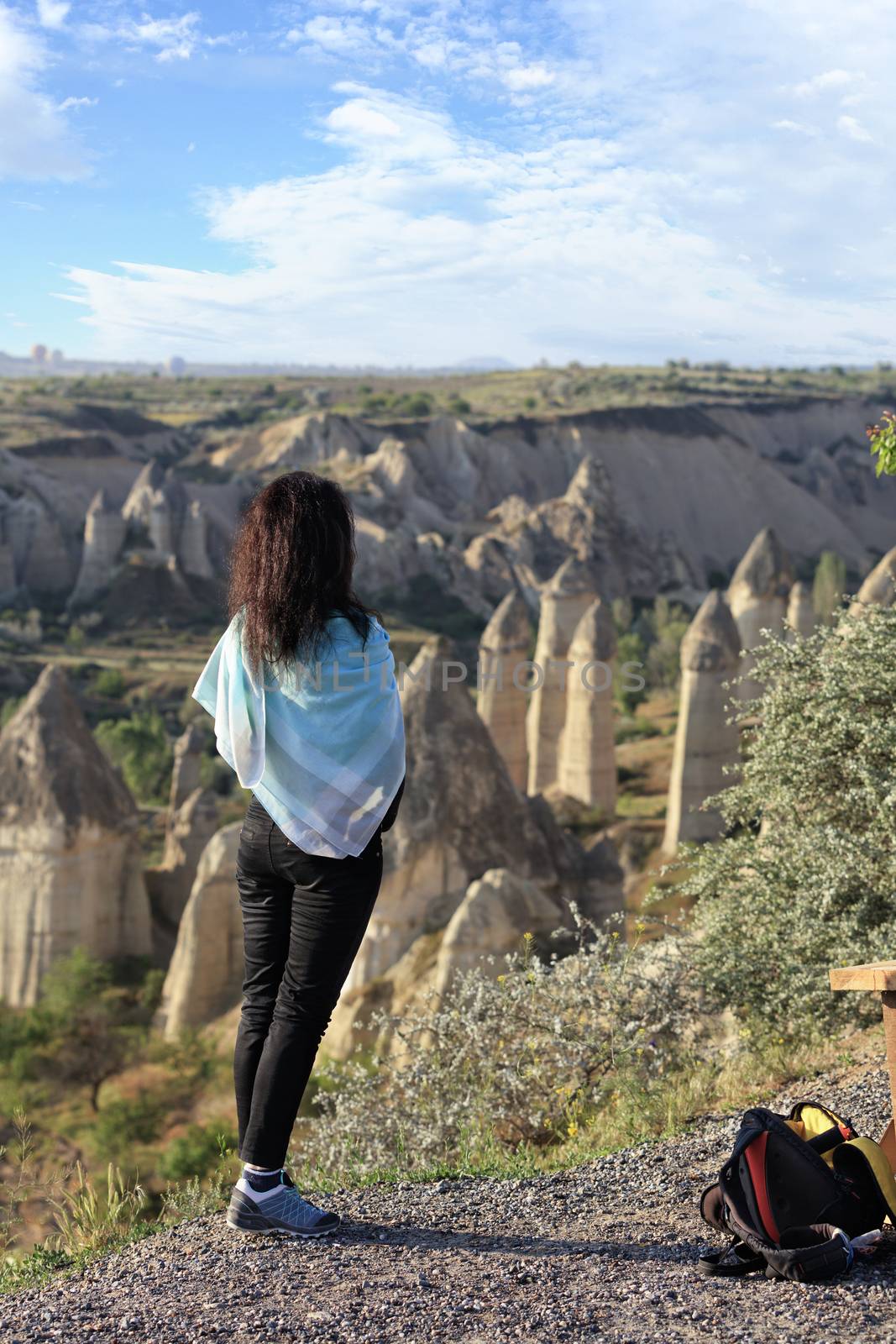 A young girl stands on the edge of a cliff and looks at the horizon, the mountain valleys of Cappadocia and the blue sky. by Sergii