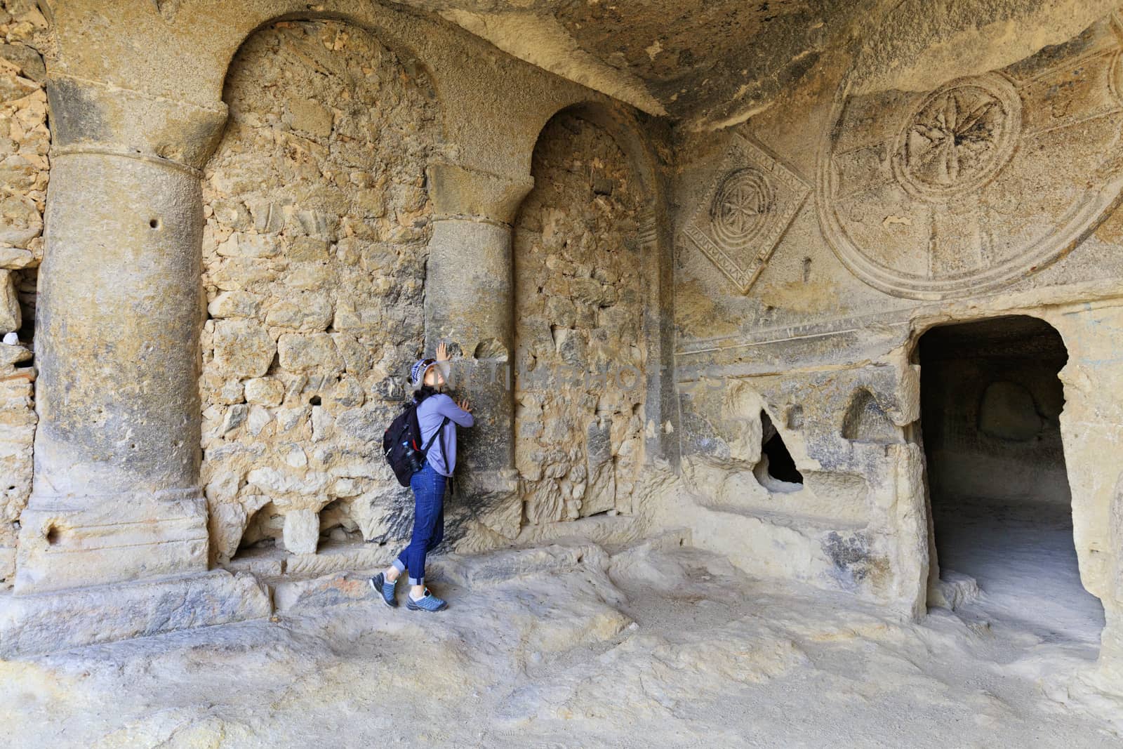 Young beautiful girl sights in the pillared hall of an old, antique, underground church carved out of sandstone rock in Cappadocia