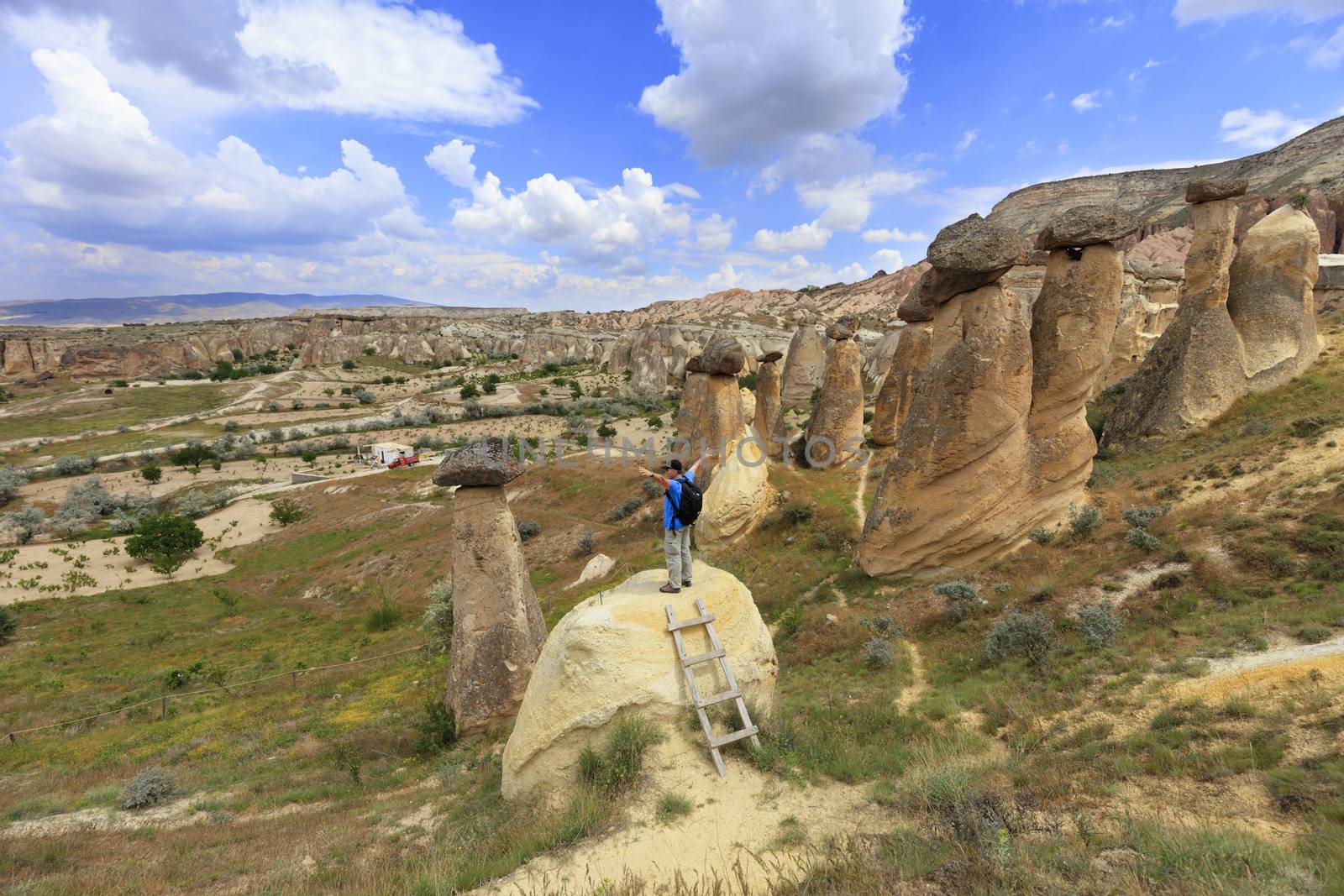 A young man stands on a rock and looks at the opening landscape and blue sky in Cappadocia. by Sergii