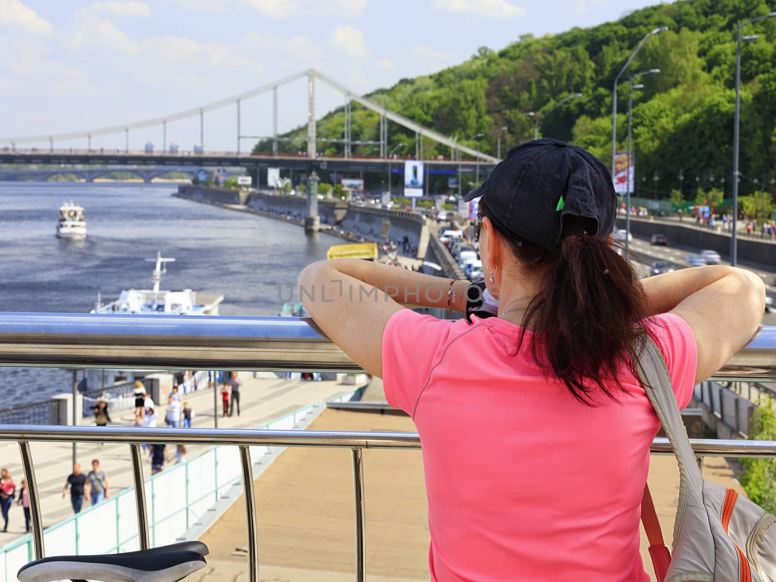 A young woman looks at the embankment of the Dnieper River in Kiev, Ukraine. A lady traveler in a bright pink T-shirt stands on the observation deck and looks towards the bridge.