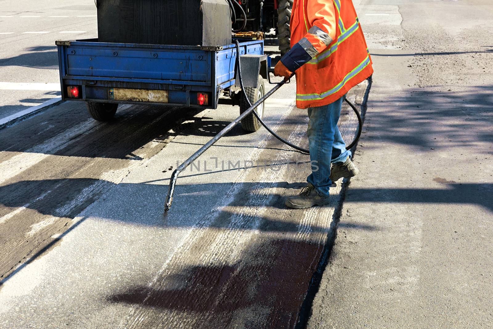 Partial repair of the asphalt road. The worker sprays bitumen on the asphalt surface by Sergii
