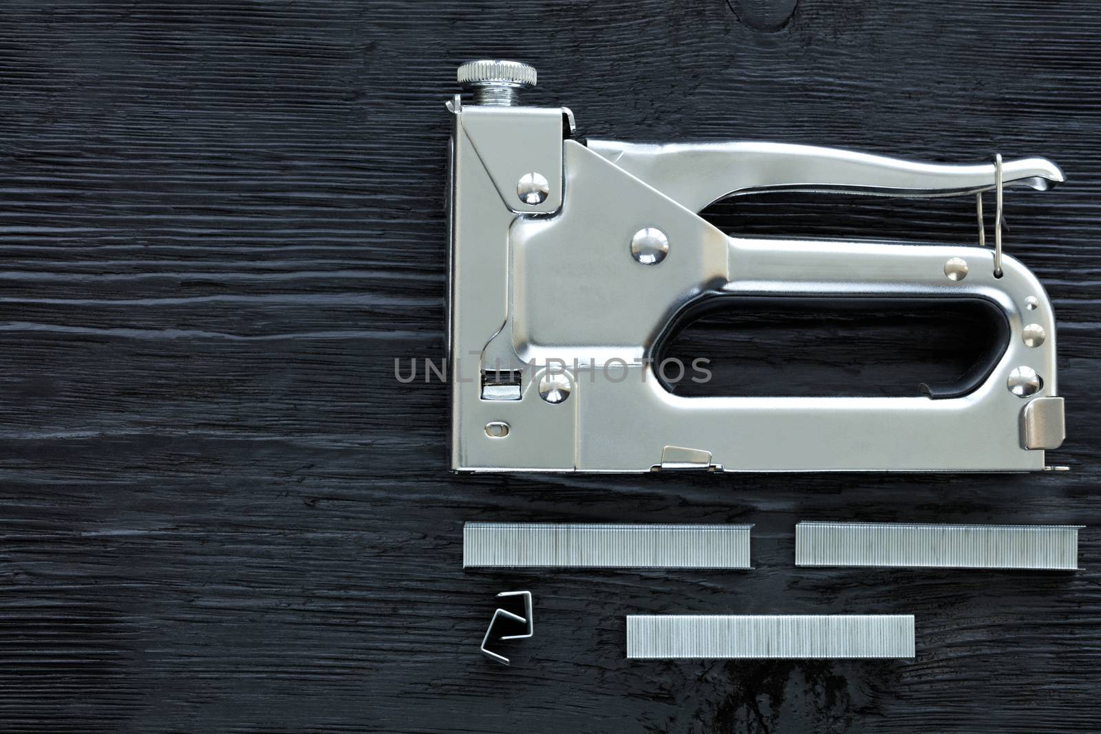 Metal industrial chrome stapler and cassette brackets to it lie on a black wooden table with the texture of old wood.