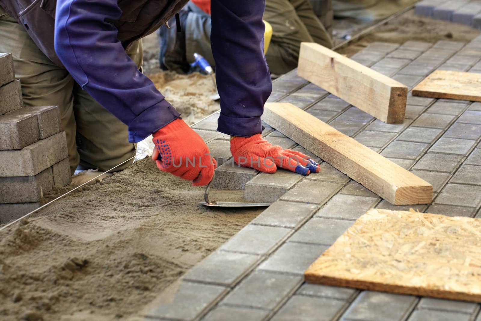 The worker levels the platform for laying paving slabs with the help of a trowel and wooden bars, aligning it to the level of the tensioned thread.