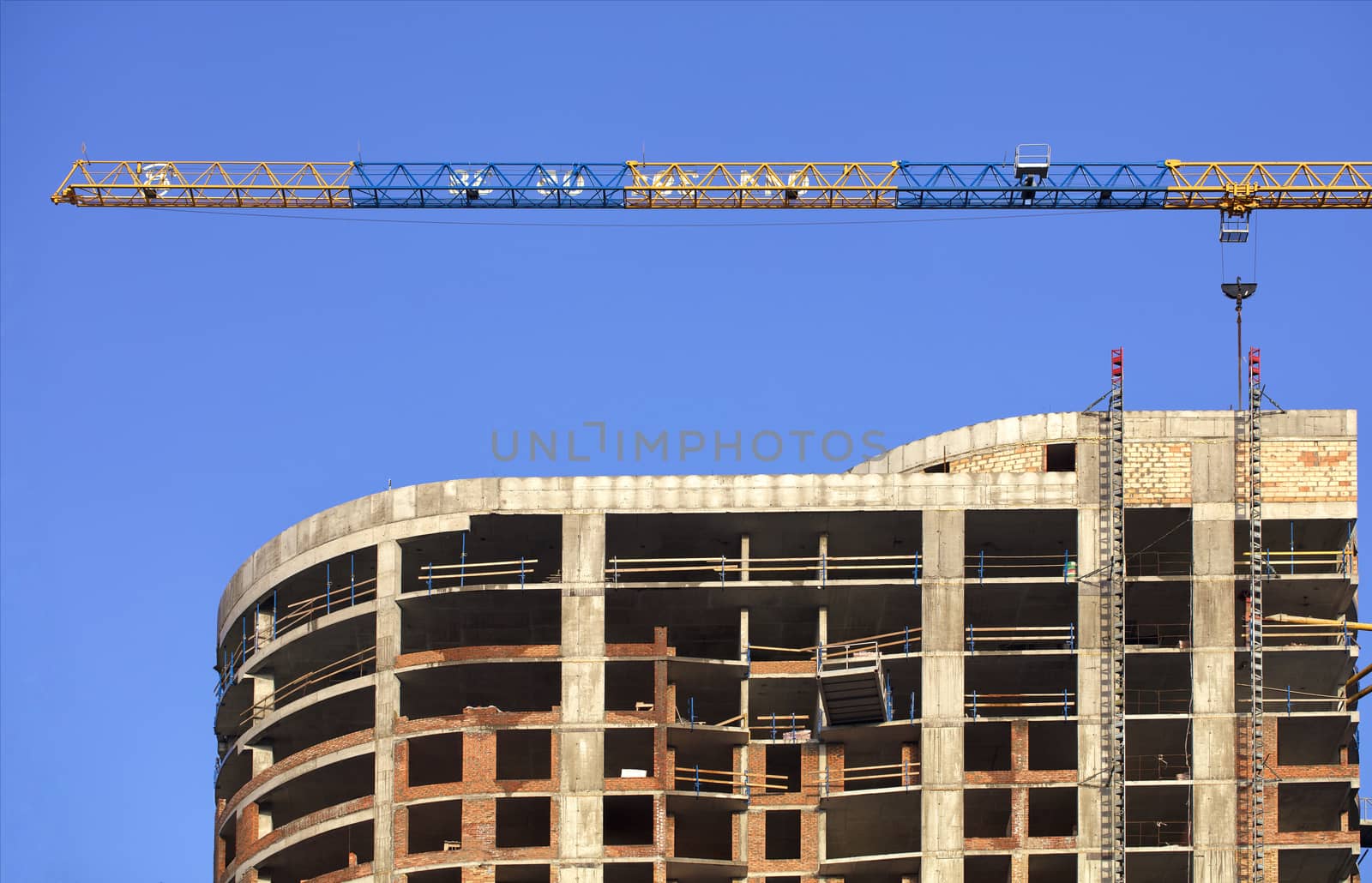 A fragment of the facade of a house under construction, a modern building is being built, an arrow of a tower crane is directed parallel to the roof against a blue cloudless sky.
