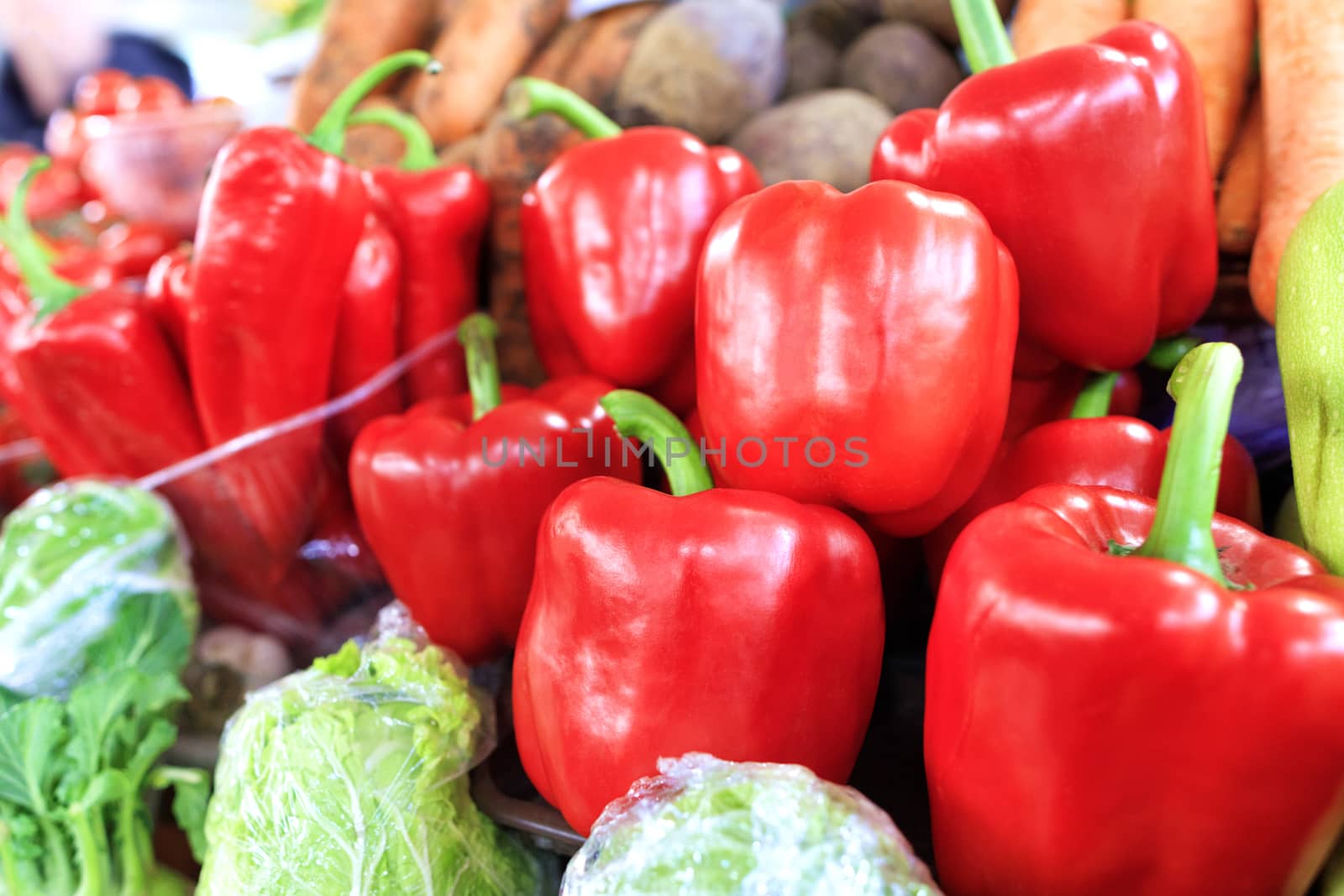 Large ripe red sweet bell peppers close-up on the background of other vegetables are sold in trays on the market in daylight.