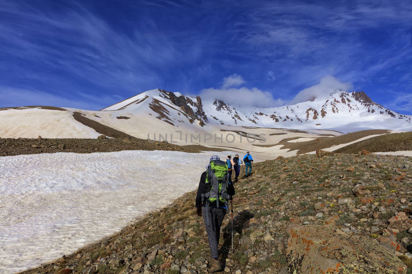 A group of tourists with backpacks behind their backs goes hiking on a rocky slope to the snow mountain Erciyas in Turkey