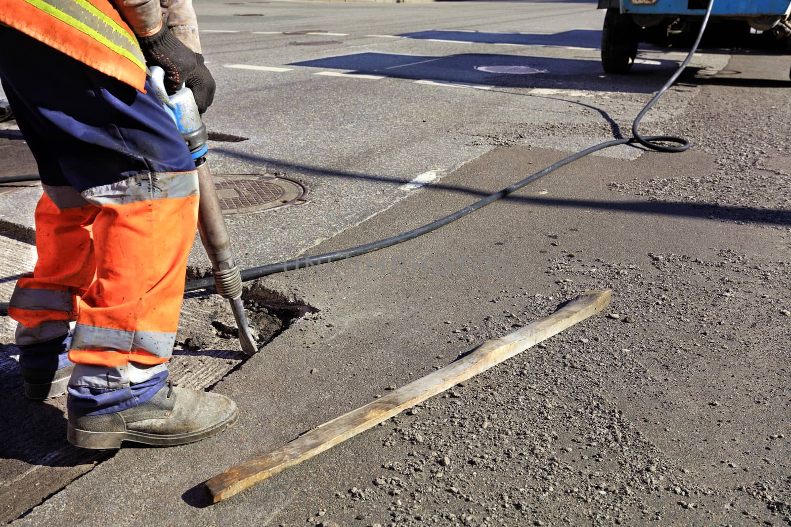 A road maintenance worker removes old asphalt on the roadway with a jackhammer into an excavator during road construction.