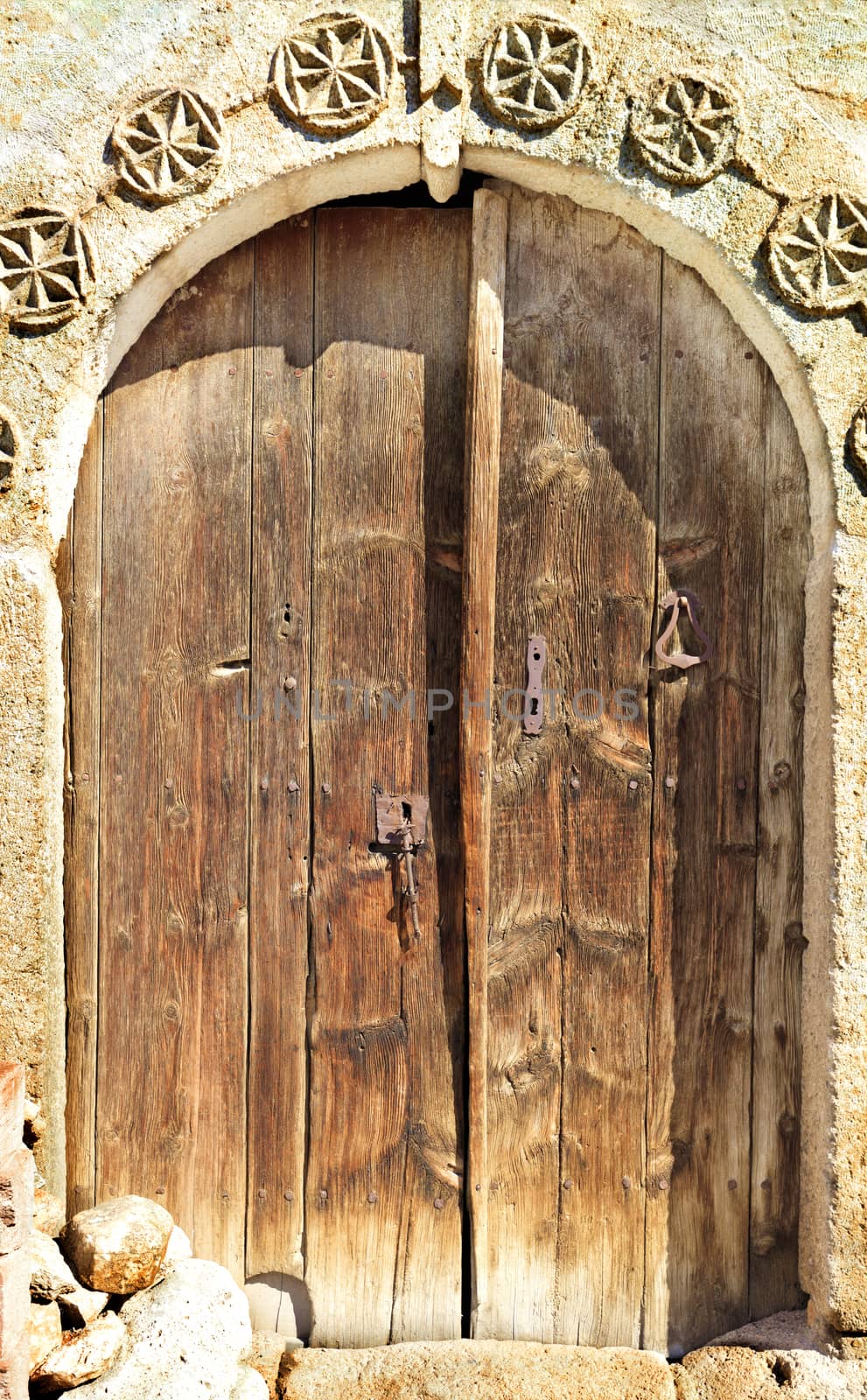 Very old weathered arched antique wooden doors with a stone pattern and metal wrought-iron lock.