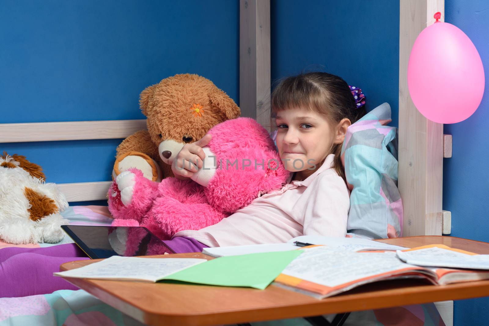 Girl's lip lying on the bed with soft toys and textbooks in the foreground