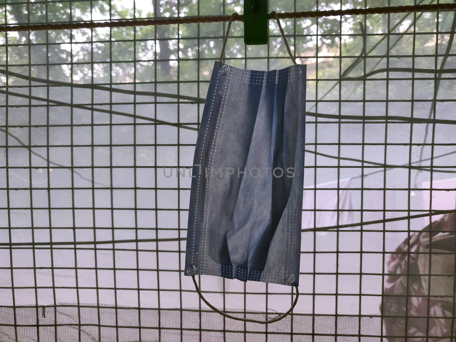 A surgical mask hanging by clothes pin near a grilled window during lock down in India