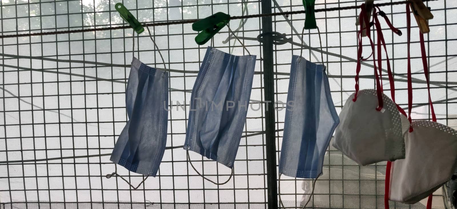 A series of N-95 and surgical mask hanging by clothes pin near a grilled window by mshivangi92