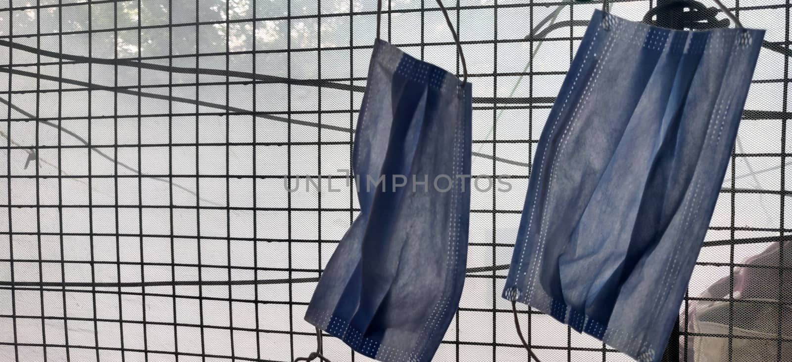 Two surgical mask hanging by clothes pin near a grilled window during lock down in India