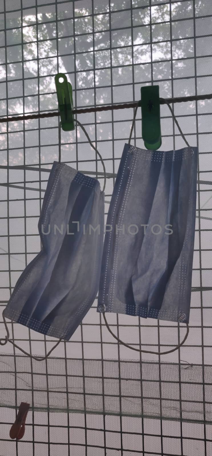 Two surgical mask hanging by clothes pin near a grilled window in a vertical photo by mshivangi92
