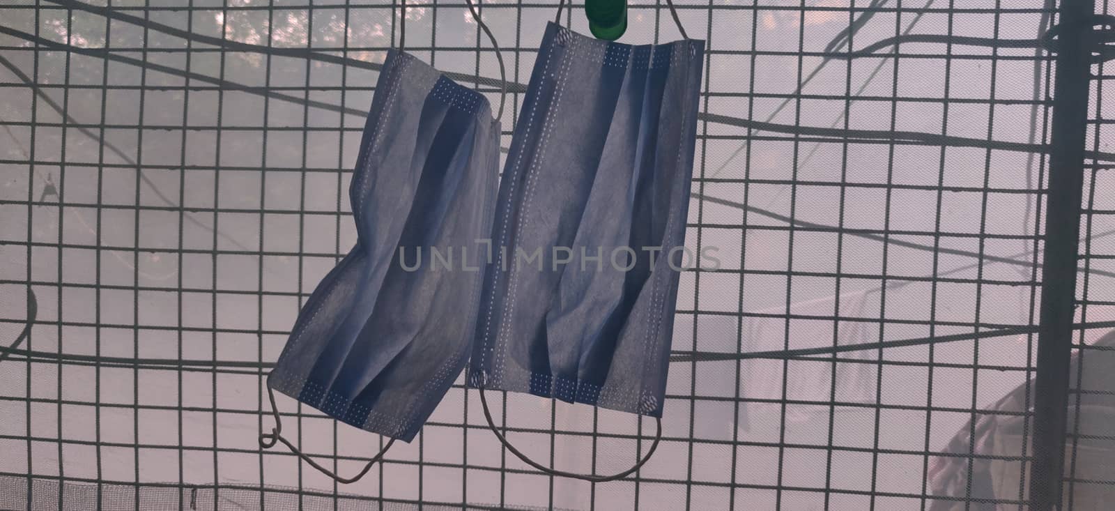 A surgical mask hanging by clothes pin against smoke near a grilled window during lock down in India