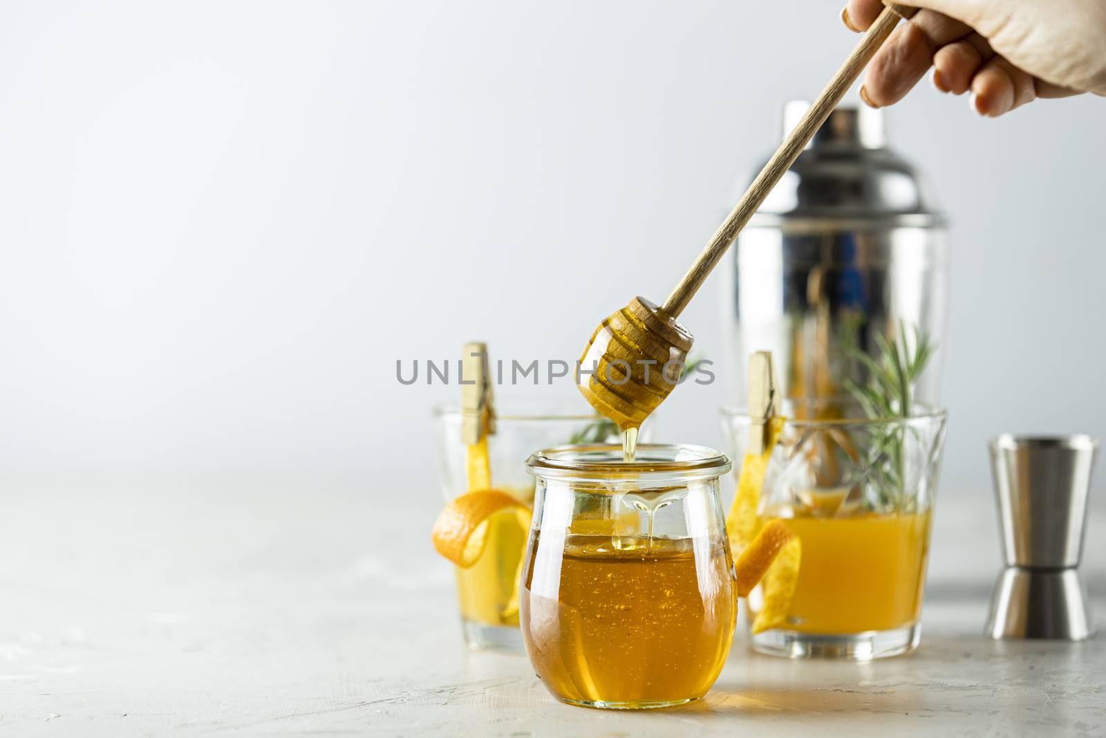Woman hand holds a spoon for honey over jar in front of two glas by ArtSvitlyna