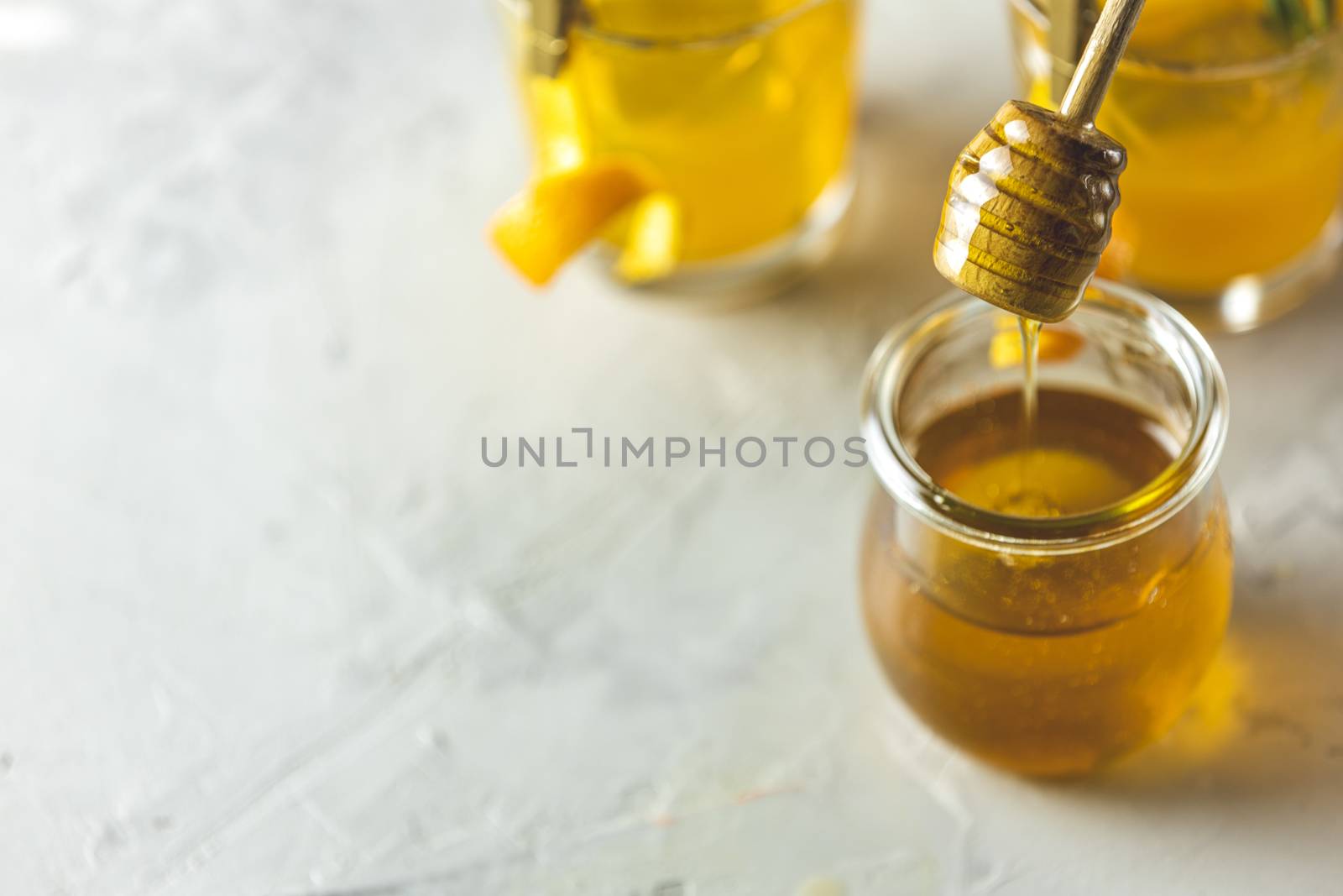 Spoon for honey over jar in front of two glasses of honey bourbo by ArtSvitlyna