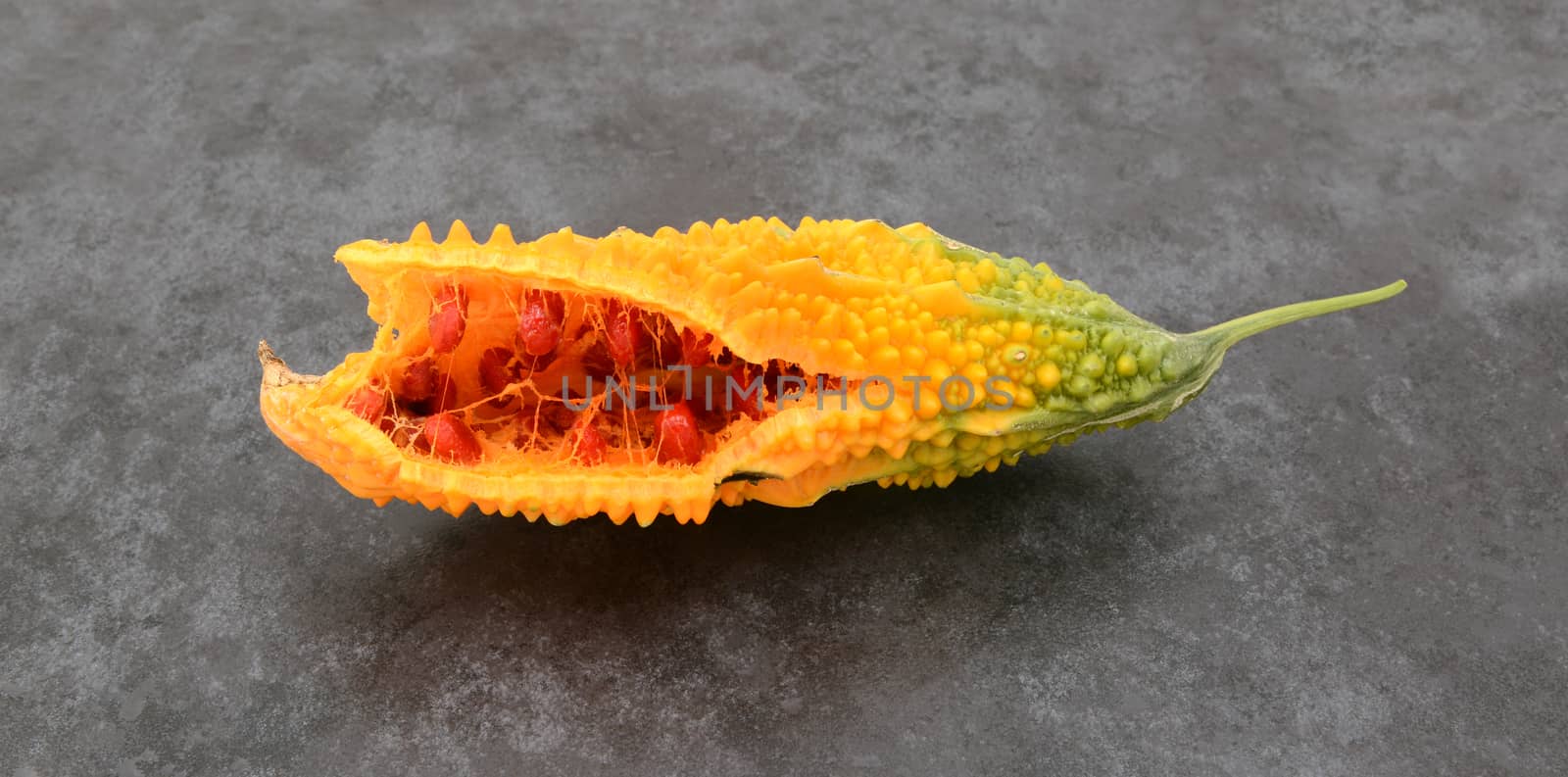 Orange bitter gourd, with ridged flesh, split open to show red seeds, on slate gray background